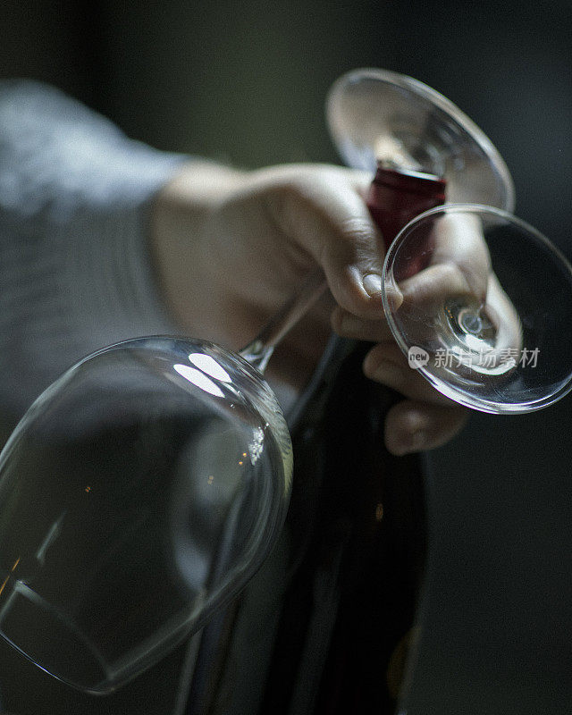 在一个小酒馆里，一个男人端着两个玻璃杯和一瓶红酒到一张桌子上。