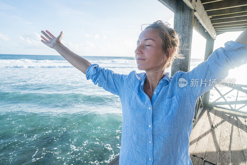 年轻女子在海上的木码头上享受海风