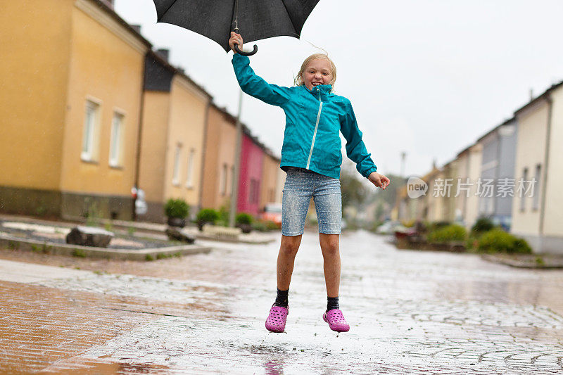 女孩有乐趣在雨天与伞跳