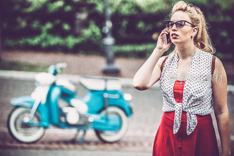 年轻女子在电话与她的老式摩托车在背景