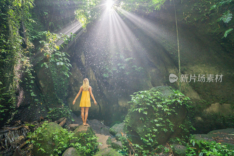 在巴厘岛的热带雨林中，旅行的年轻女子张开双臂拥抱大自然的美丽。人们以自然为旅游理念。