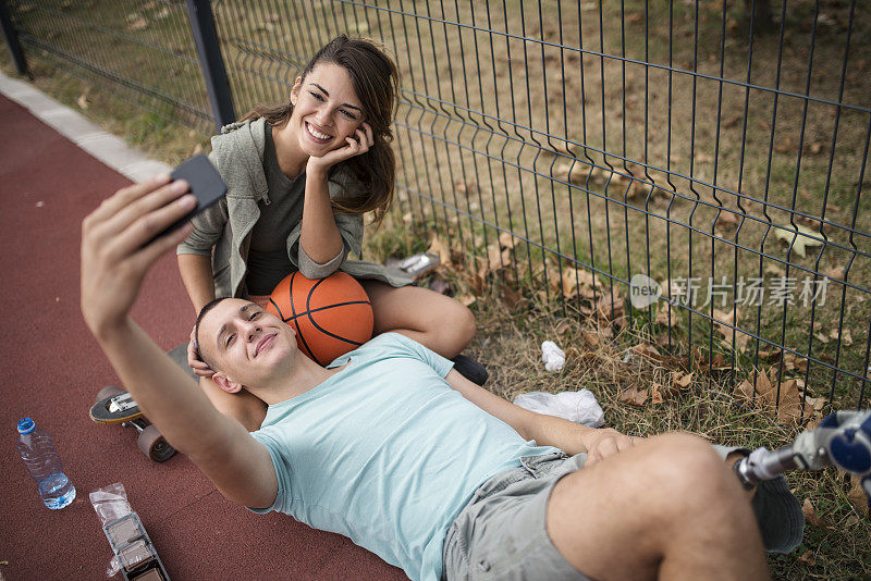 一对年轻情侣躺在篮球场上自拍