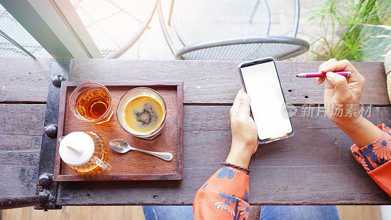 一位女士在咖啡馆的咖啡桌上使用智能手机，智能手机的白屏