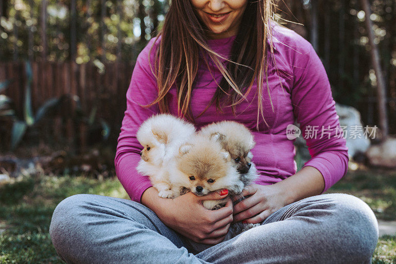 微笑的年轻女子坐着，抱着她的博美犬