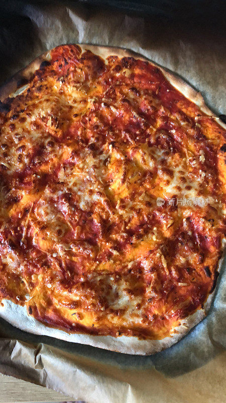 这是在厨房烤箱中烘焙的自制披萨食谱，在披萨石上烤成薄而脆的披萨底，烧焦的意大利那不勒斯玛格丽特披萨，上面铺有磨碎的马苏里拉奶酪，番茄酱，意大利香草，新鲜的罗勒叶
