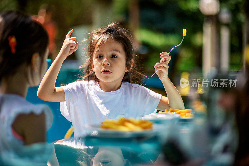 两个小女孩用叉子吃薯条，互相聊天