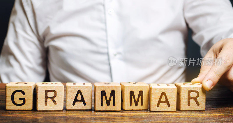 一个人把单词Grammar放在木块上。在一种自然语言中，控制子句、短语和单词组成的一套结构规则。音位学，形态学，句法，语音学