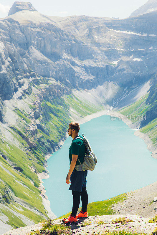 在阳光明媚的夏日里，一名年轻的背包客在瑞士阿尔卑斯山徒步旅行