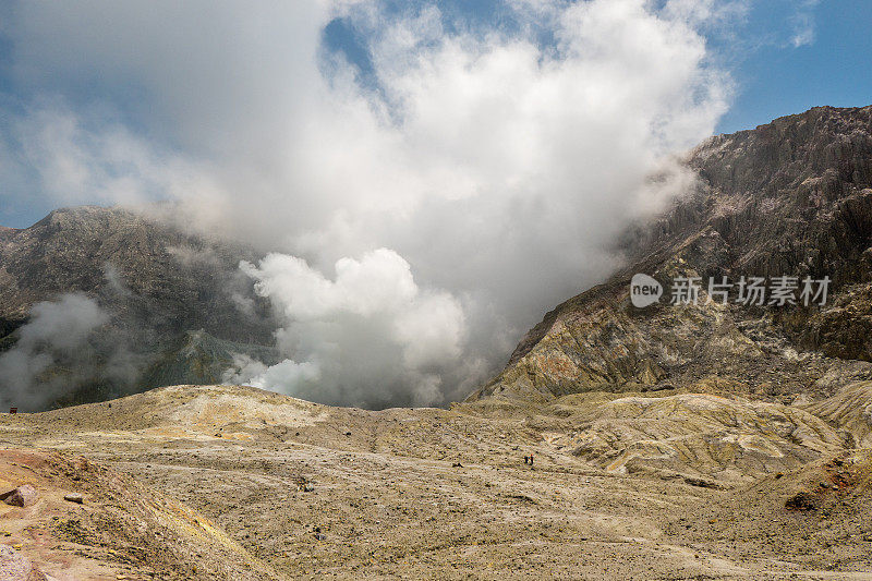 新西兰的怀特岛火山，望向火山口。远处，两位火山学家正在熔岩平原上行走。