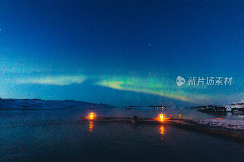 在冰岛，一名男子在冰湖和雪山上享受北极光，他在温泉池中沐浴