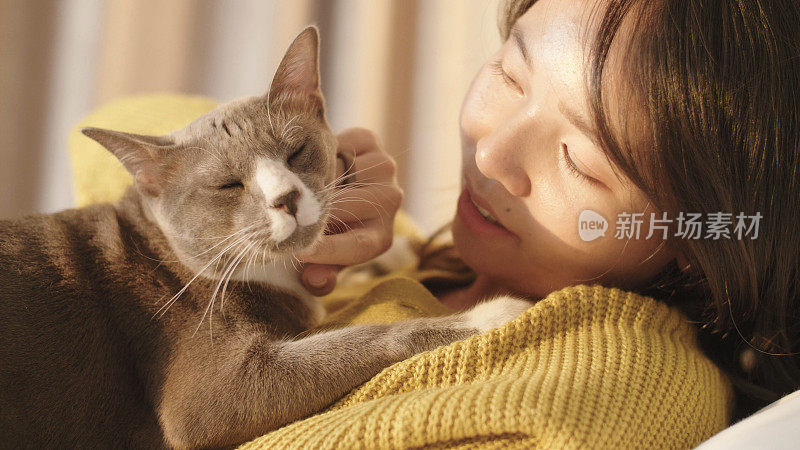 一个年轻女子在卧室白色的床上玩她的宠物猫。