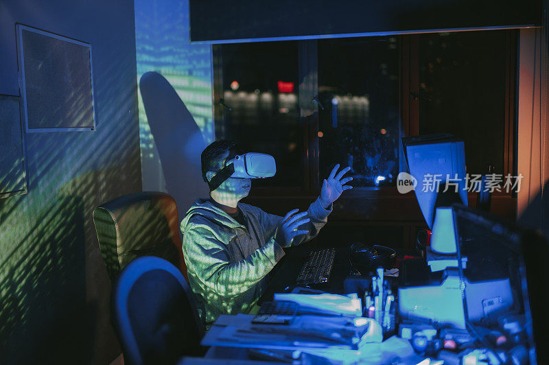 一名亚裔中国男性，晚上在他的家庭办公室自习室，戴上VR眼镜，在他的台式电脑前体验3D虚拟游戏