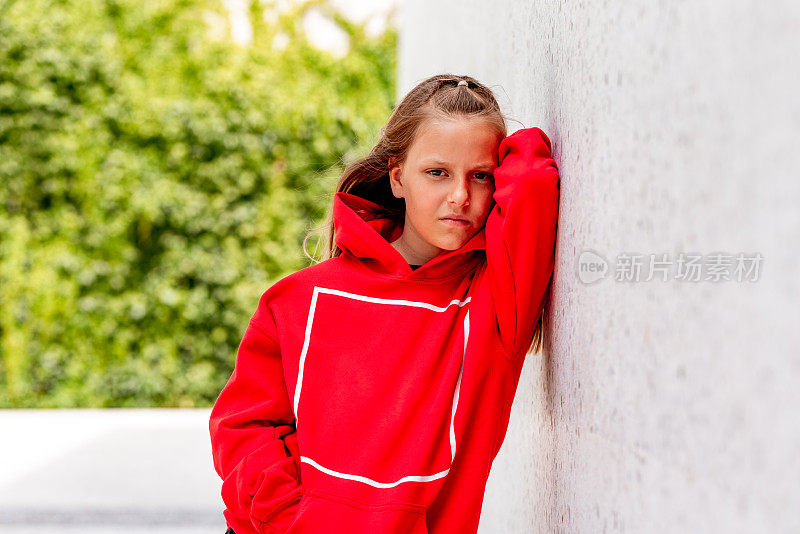 一个年轻的女孩靠在外面的白色混凝土墙上