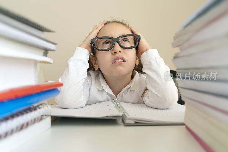 一个又烦又累的小女孩在书桌上拿着书做作业