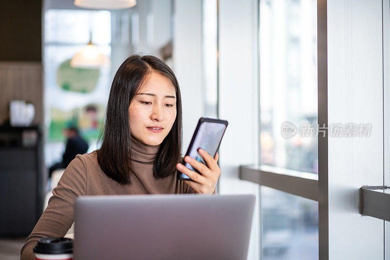 年轻的亚洲女性在咖啡店使用智能手机和笔记本电脑