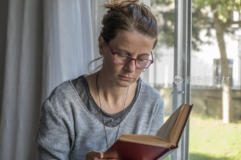 戴眼镜的女人在窗前看书