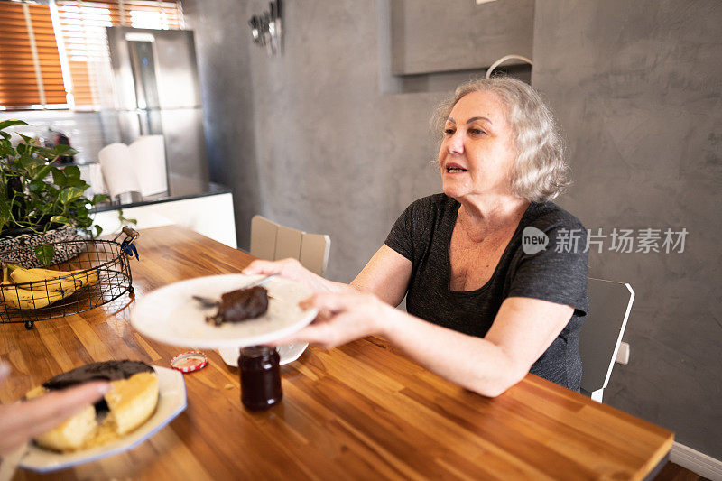 年长的女人在和朋友喝下午茶时提供蛋糕