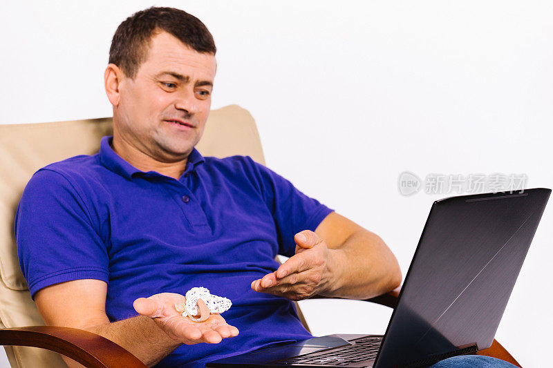 一个有听力障碍的白人聋人拿着一个助听器给笔记本电脑的摄像头看。美国手语交谈在线