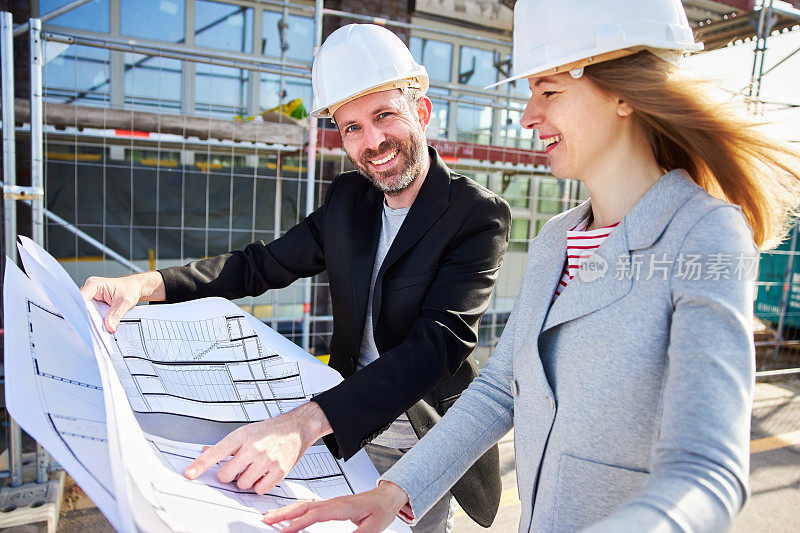 建筑师或土木工程师在施工现场与客户或同事一起查看规划文件或技术图纸，两人都戴着白色安全帽