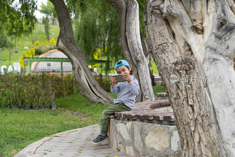 男孩坐在公园里用手机看视频