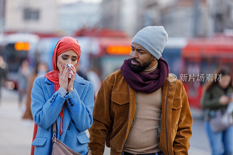 一位患季节性流感的妇女和她的丈夫在市区散步，并用纸巾咳嗽。