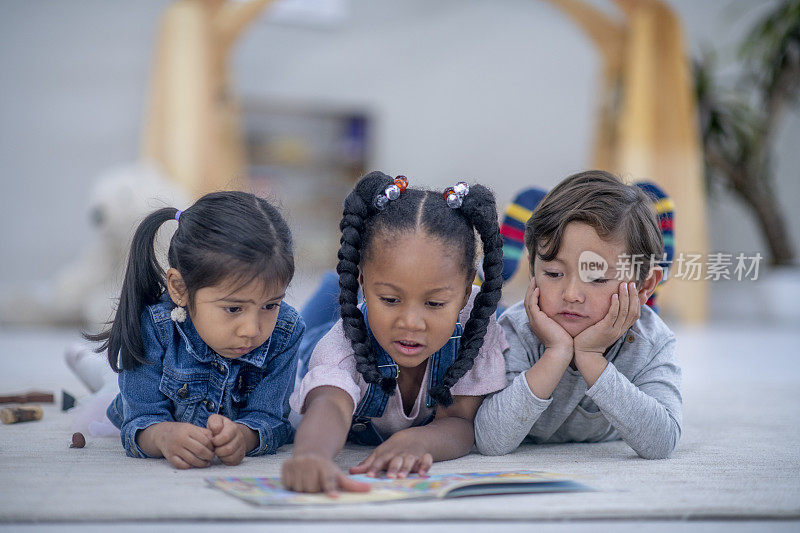 三个多民族学龄前儿童在读一本书