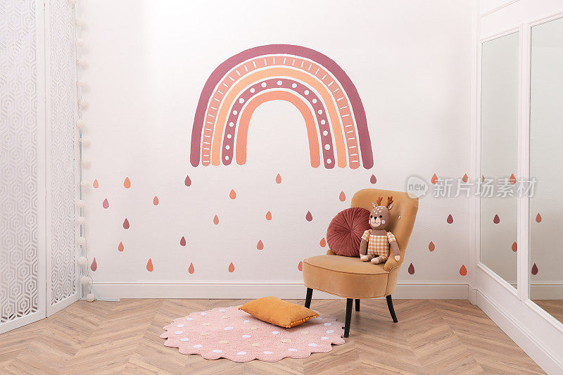 儿童房内部有舒适的扶手椅、玩具和白色墙壁上的绘画。时尚的设计