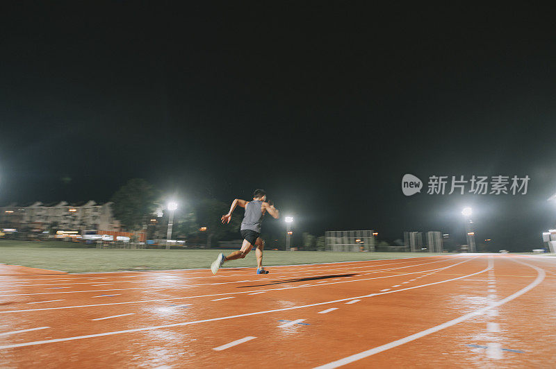 亚洲华人男运动员雨夜在田径场跑道上冲刺，向终点跑去