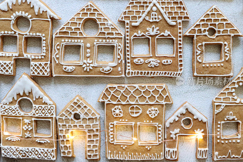 近距离拍摄成排自制的房子形状的姜饼饼干，被童话灯照亮的白色糖霜饼干，圣诞村展示，大理石效果背景，高架视野