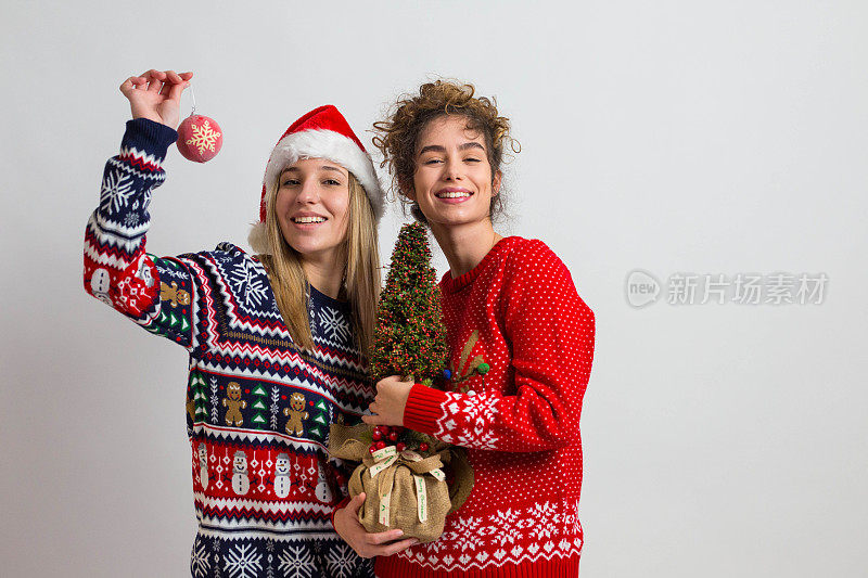 这是我的圣诞礼物!两个漂亮的女孩穿着新年毛衣，带着新年礼物