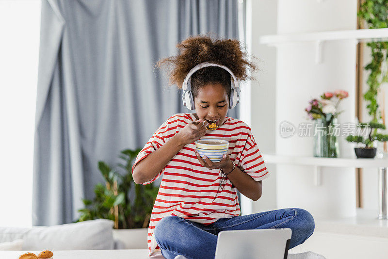 可爱的女孩看互联网内容的数字平板电脑和吃早餐在家里