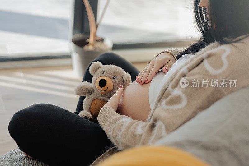 孕妇抱着泰迪熊在沙发上摸肚子