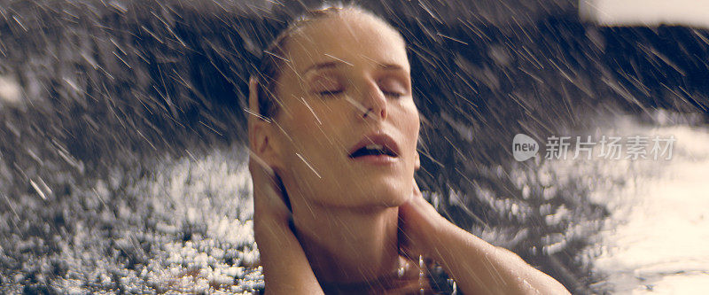 自然的女人从水里冒出来，享受着雨。轻轻地抚摸着她的脸和长发。美容护理的比喻