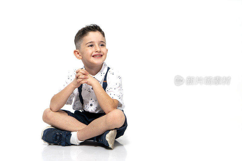 可爱的小男孩坐在白色背景的地板上，自信，坚定，微笑着