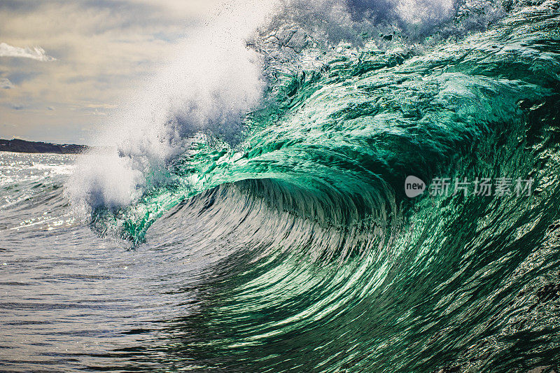 强大而明亮的蓝绿色海浪在浅滩礁石上翻滚的特写