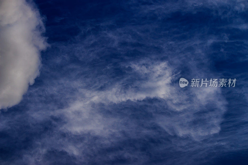 图片左侧是白色蓬松的积云，背景是深蓝色的天空，被旋涡风吹起的卷云。