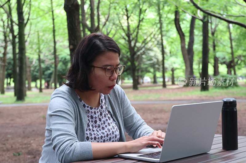 一个年轻女子坐在公园的户外，手里拿着一台笔记本电脑