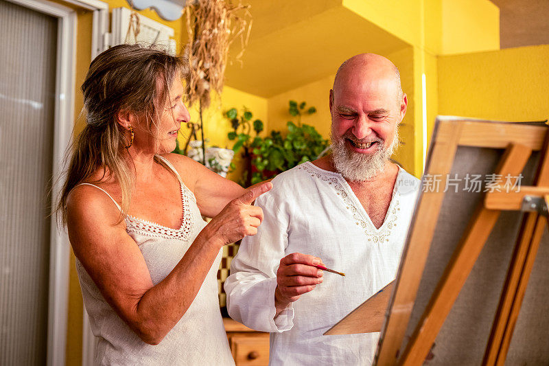 一对自信、快乐的老年夫妇在客厅里画画，享受着他们的闲暇时光和生活