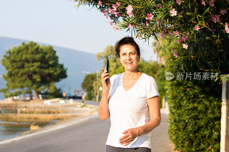 海岸线上拿着智能手机的成熟女子