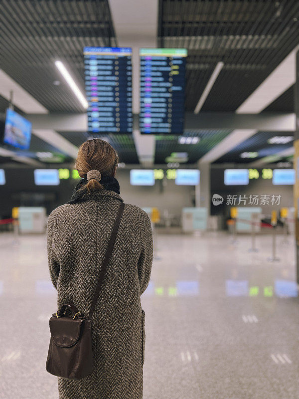 冬季，一名女子在机场注视着到达和离开的登机牌。