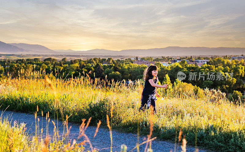 快乐的微笑的女孩嬉戏在夕阳下的荒野农村草地户外