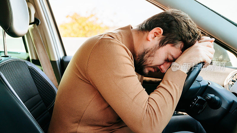 疲惫的年轻司机睡在他的车里，他的头在方向盘上。