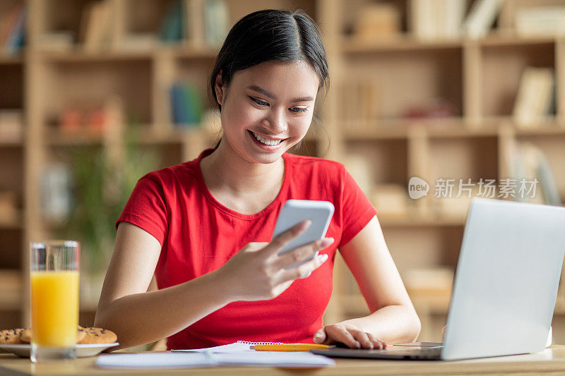 快乐的青春期中国女学生在房间内部的电脑桌上用智能手机打字
