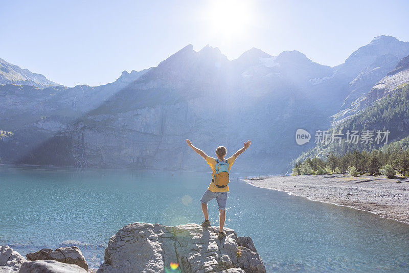 人们在夏天凝视着美丽的自然，他双臂伸开站在高山湖边的岩石上