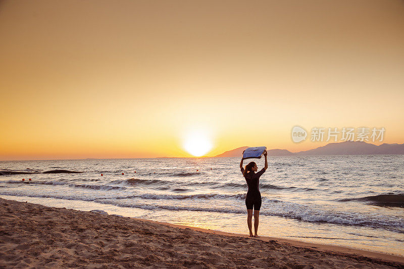 剪影的年轻女子在潜水服携带冲浪板以上的头