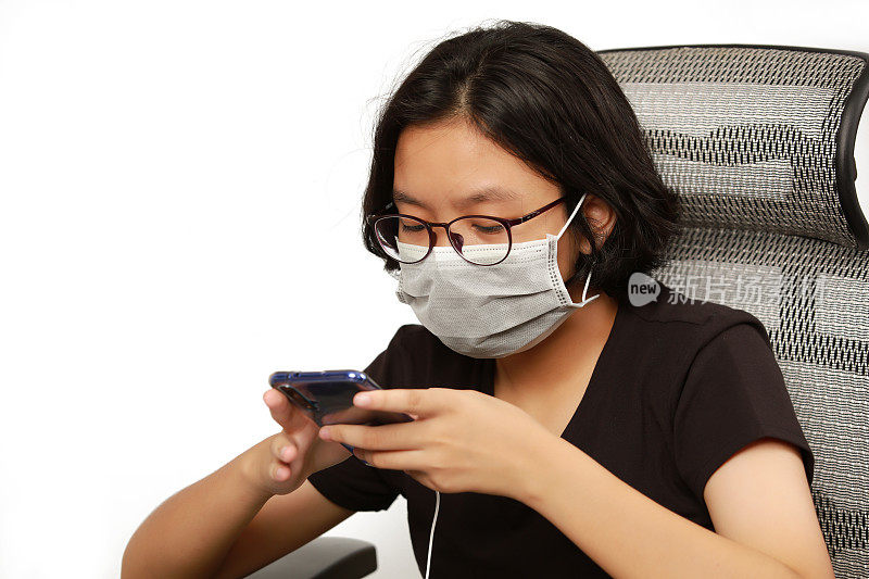 女孩戴着卫生口罩玩智能手机，新冠疫情后的新常态生活方式