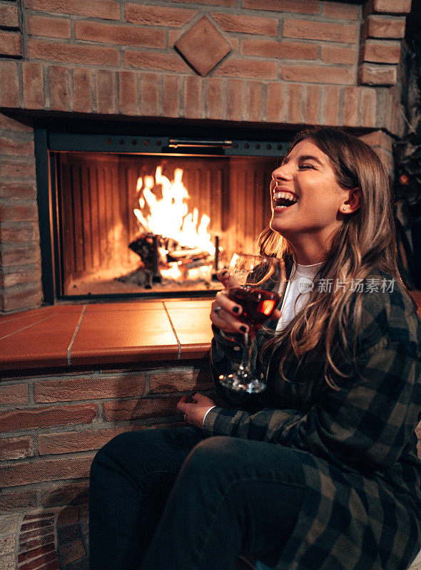 幸福的女人端着酒杯在壁炉边笑