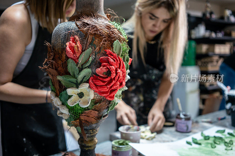 浮雕花瓶是前景，重点是前景，两位女艺术家是背景水平艺术家