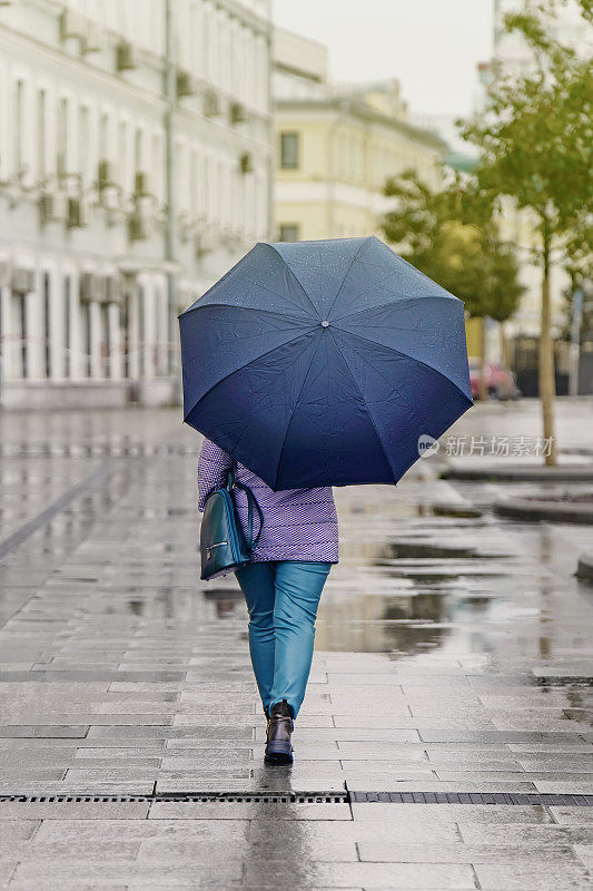 女孩撑着伞走在城市潮湿的人行道上