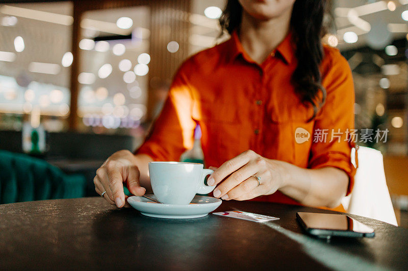 一个中年妇女在当地一家咖啡馆放松时，手拿着咖啡杯的特写